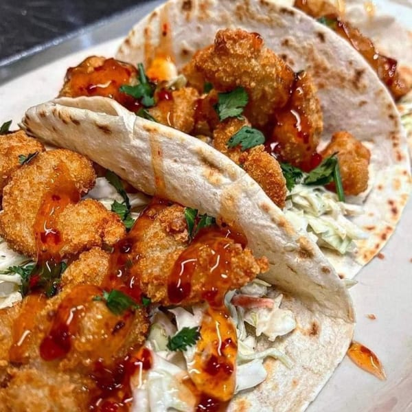 Close-up of two Stadium 34 crispy shrimp tacos with slaw, cilantro, and sweet chili sauce.