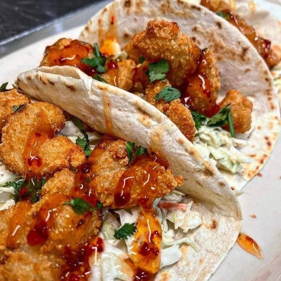 Close-up of two Stadium 34 crispy shrimp tacos with slaw, cilantro, and sweet chili sauce.