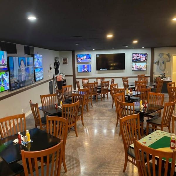 Interior of Stadium 34, an American restaurant, with multiple TVs showing sports and news, and wooden tables and chairs.