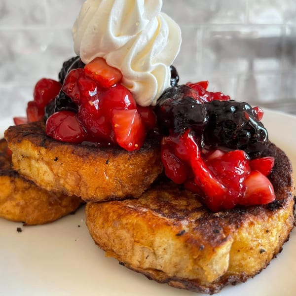 Golden French toast topped with whipped cream, fresh strawberries, and mixed berries.
