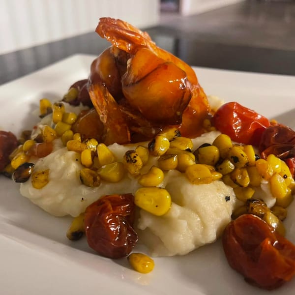 Shrimp and grits with roasted corn and cherry tomatoes on a white plate.