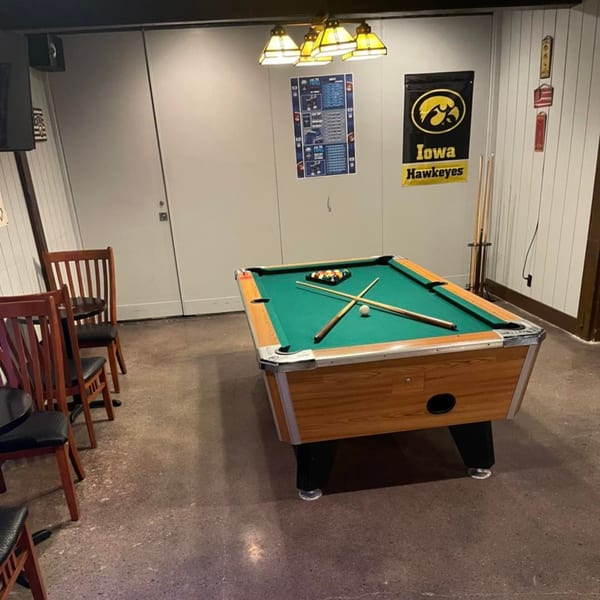 A pool table with cues and balls, chairs, and Iowa Hawkeyes banner in a game room.