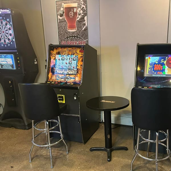 Arcade games and bar stools in Stadium 34, with a dartboard and football poster.