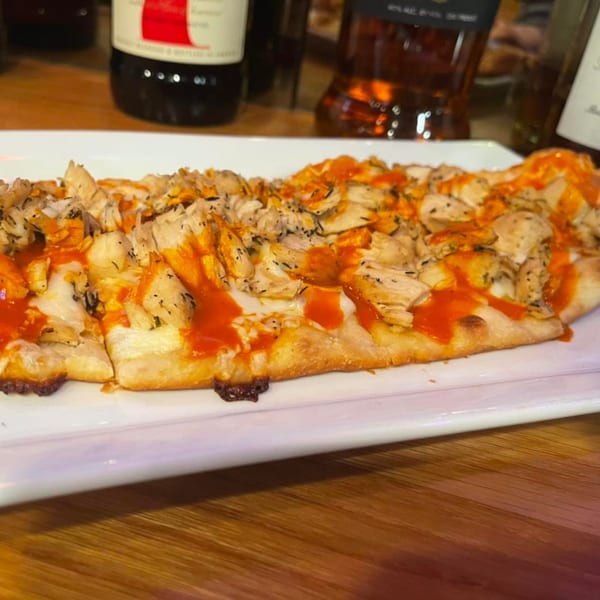 Buffalo chicken flatbread with cheese and red sauce on a white rectangular plate.