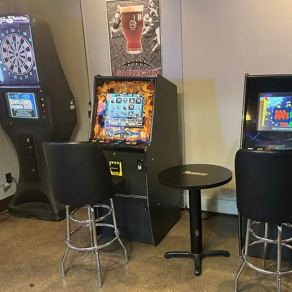 Arcade games, including a dartboard and slot machines, with bar stools and a small table.