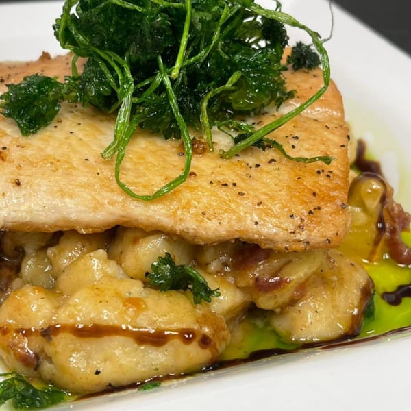 Pan-seared fish fillet with crispy greens, gnocchi, and a rich sauce on a white plate.